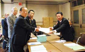 杉山健康福祉局長に署名用紙を提出する久野議員と奥村本部長